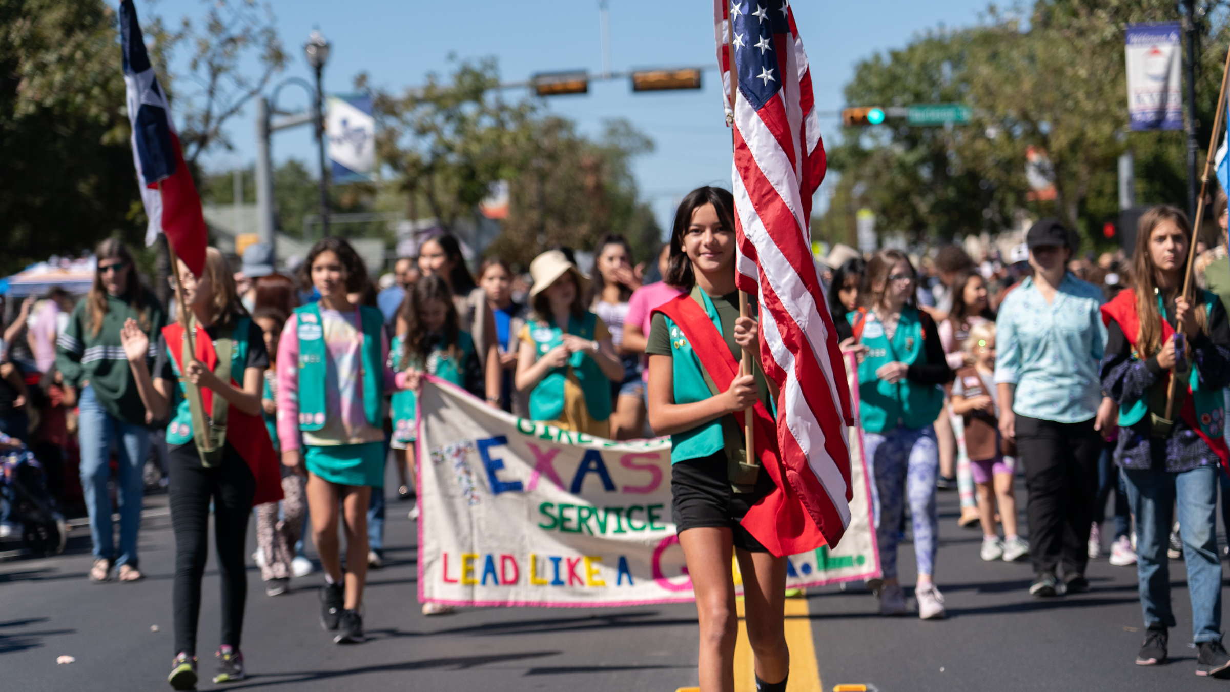 A group of Girls Scouts walk in a parade with one young girl in the foreground carrying an American flag. 