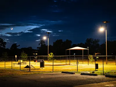 A sliver of the moon is visible between the clouds at night as lights shine on the Steeplechase Dog Park in Kyle, TX.