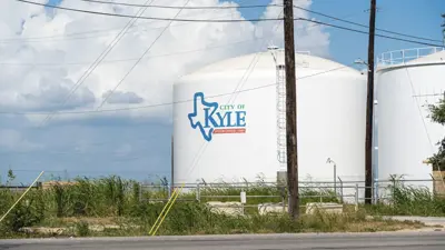 A picture of a large white water tank next to another white water tank that says City of Kyle during a beautiful sunny day with blue skies and fluffy white clouds. 