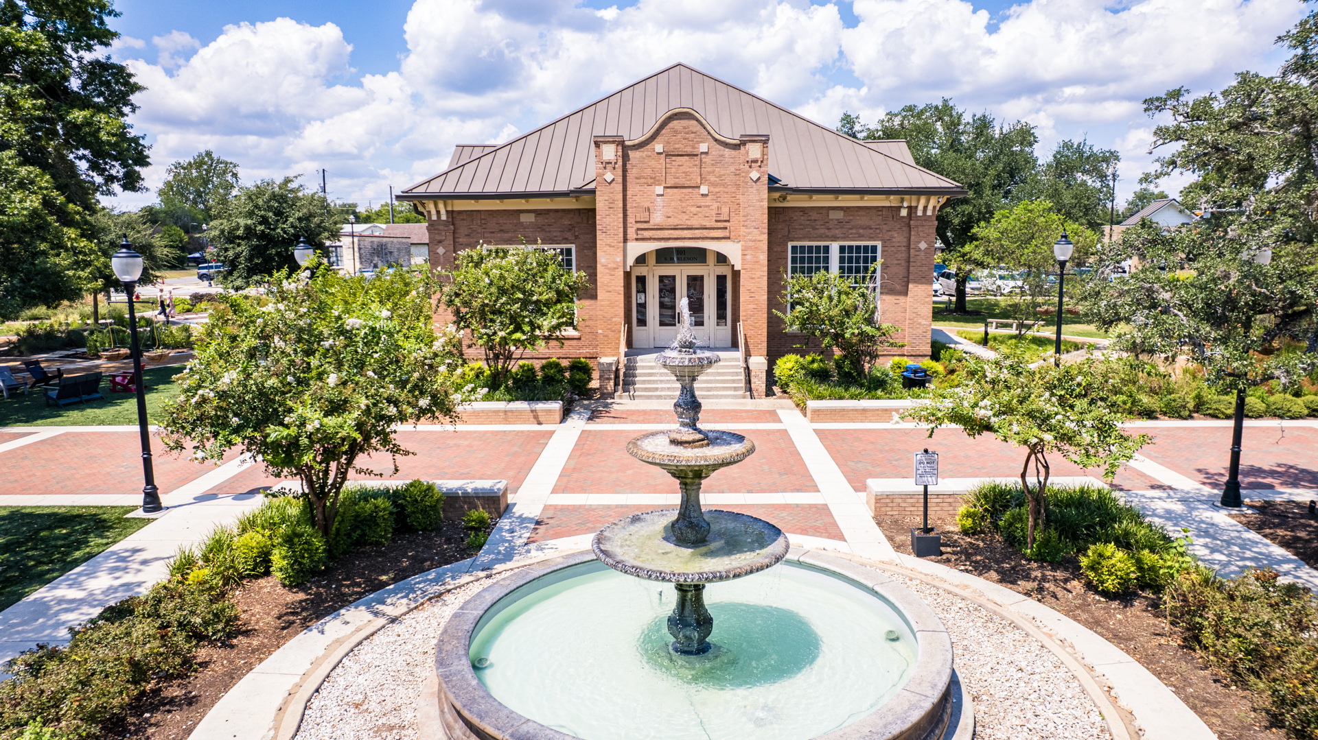 Tiered water fountain in front of brick building surrounded by trees