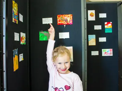 Young girl standing in front of paintings and pointing up