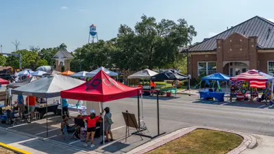 Tents line Burleson Street in downtown Kyle as part of a previous Market Days event. The Krug Activity Center and water tower can be seen in the background. 