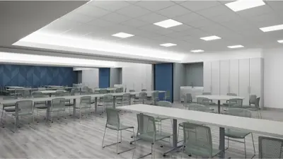 A large multipurpose room with rows of tables and chairs, built-in storage cabinets, and open floor space designed for classes, events, or group activities.