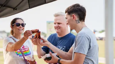 Three people stand together and cheers their ribs at the Kyle Fair at Lake Kyle Park. 
