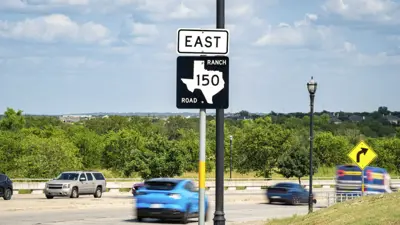  A photo of a black and white TXDoT sign that says FM 150 with cars going by some of which are blurred due to the lens capture. 