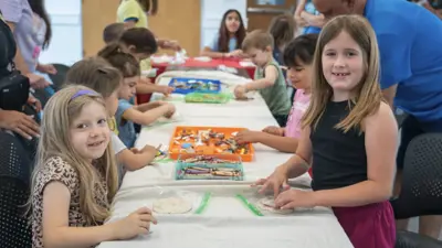 Two young girls smile at the camera while working on an arts and crafts project at the Kyle Public Library. 