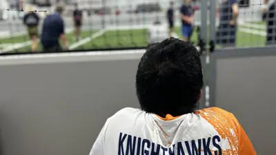 A picture of a City of Kyle special olympics athlete looking at a bocce field with 'KNIGHTHAWKS' written on the back of his orange and white jersey. 