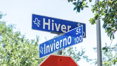 A photo of two street signs, Hiver St. and Invierno St., in Kyle, TX that are blue in color with white text over a red stop sign. 