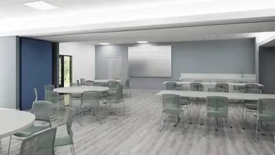 A flexible meeting room with round and rectangular tables, movable chairs, a serving counter, and large windows providing natural light.