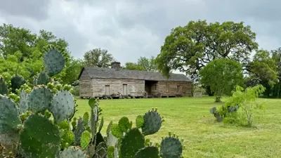 A picture of the Claiborne Kyle Log House with cactus in the forefront. 